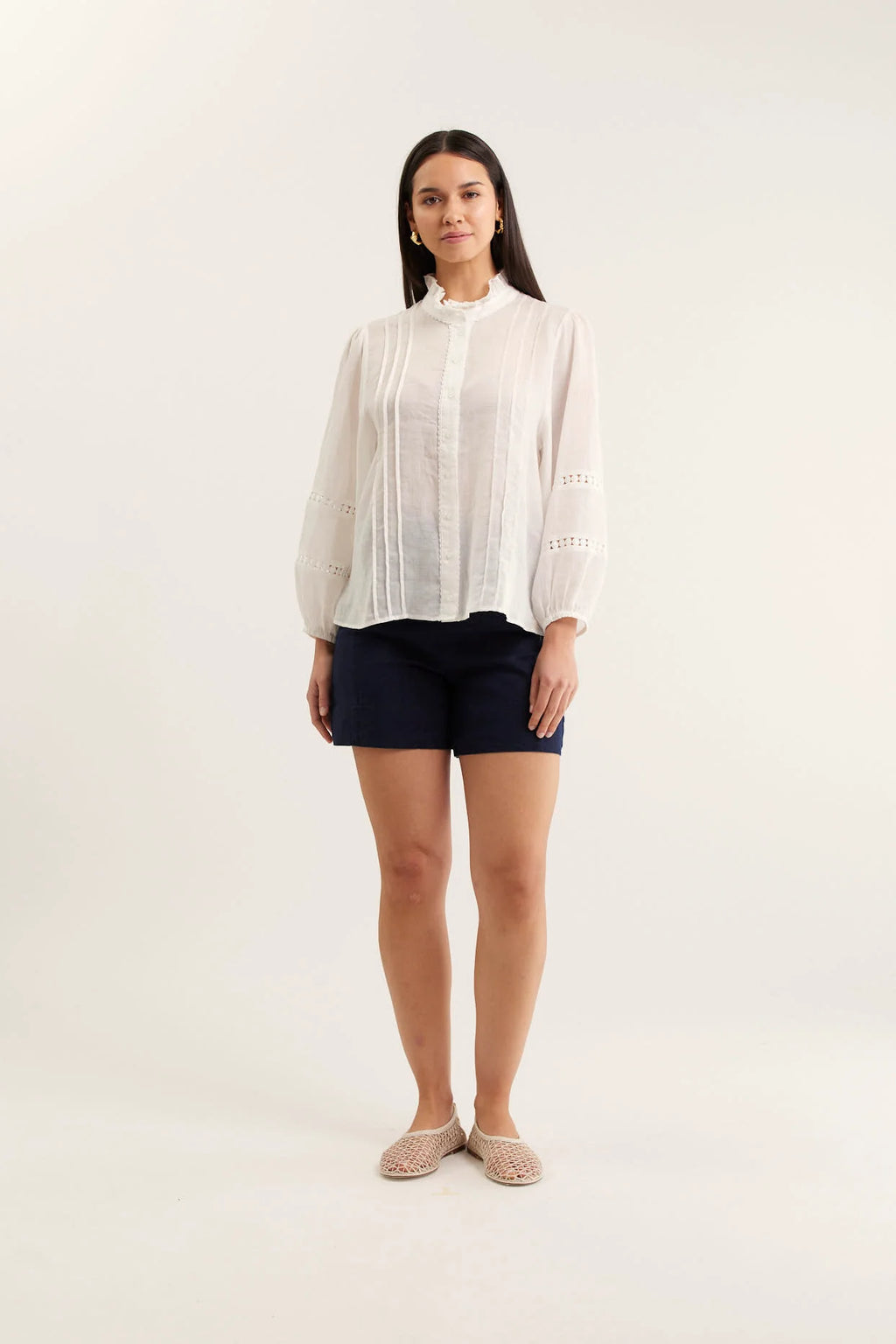 Woman wearing a white blouse and navy shorts on a white background