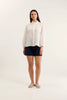 Woman wearing a white blouse and navy shorts on a white background