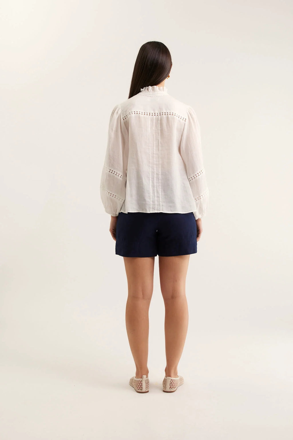 Person wearing a white blouse and navy shorts on a plain background