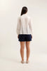 Person wearing a white blouse and navy shorts on a plain background