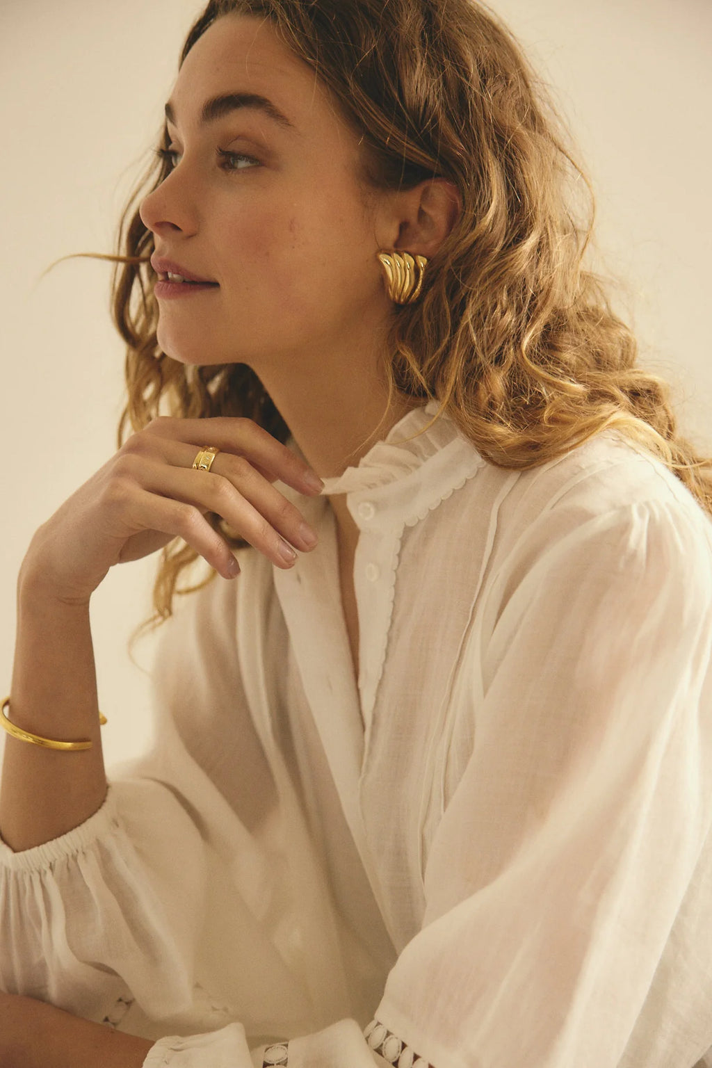 Woman wearing gold earrings and a ring, with a plain background