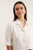 Woman wearing a light-colored shirt with a collar against a plain background