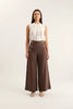 Woman wearing a white sleeveless top and brown wide-leg pants with gold buttons on a white background