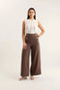 Woman wearing a white sleeveless top and brown wide-leg pants with buttons on a white background