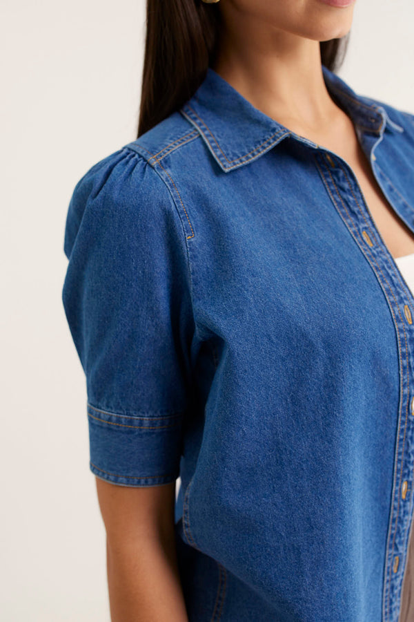 Blue denim shirt worn by a person on a plain background