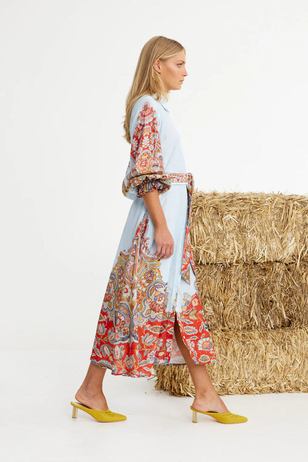 Woman wearing a colorful dress standing next to hay bales on a white background