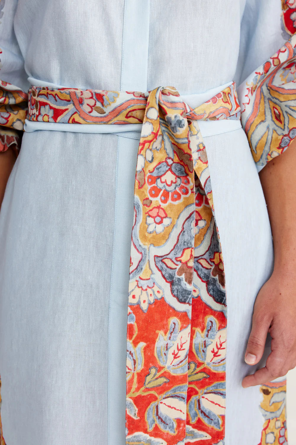 Colorful patterned belt tied around a light blue dress with floral design.