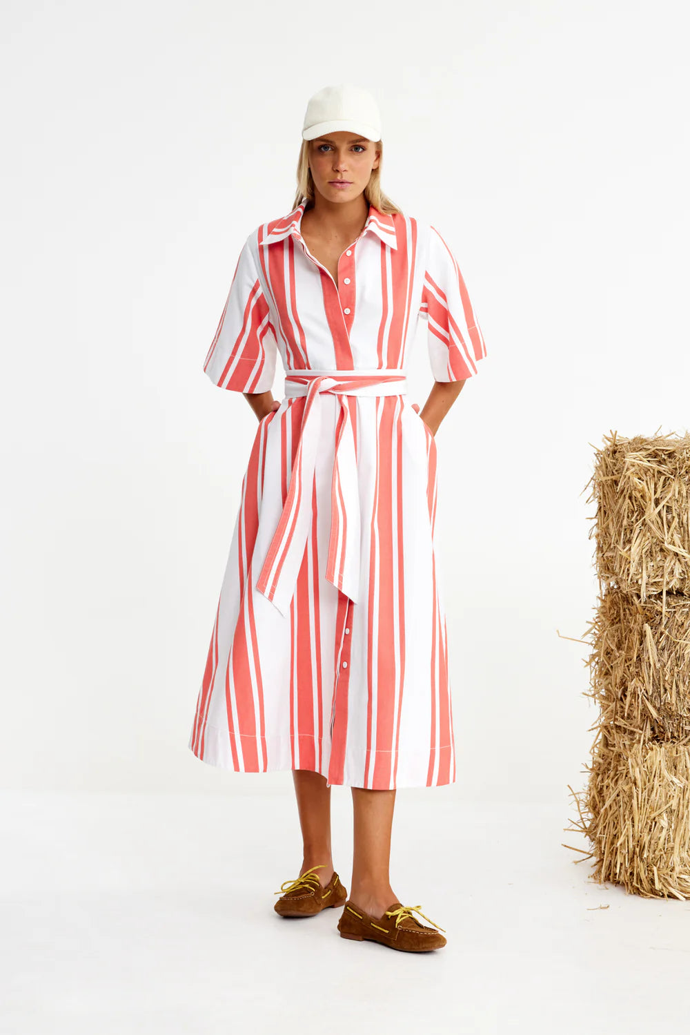 Woman wearing a red and white striped dress standing next to a bale of hay.