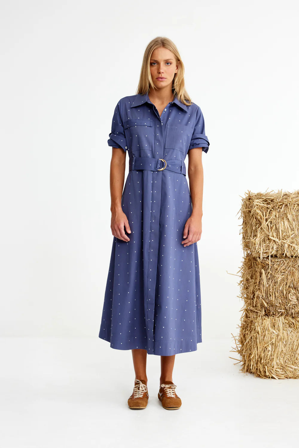 Woman wearing a blue dress standing next to hay bales on a white background