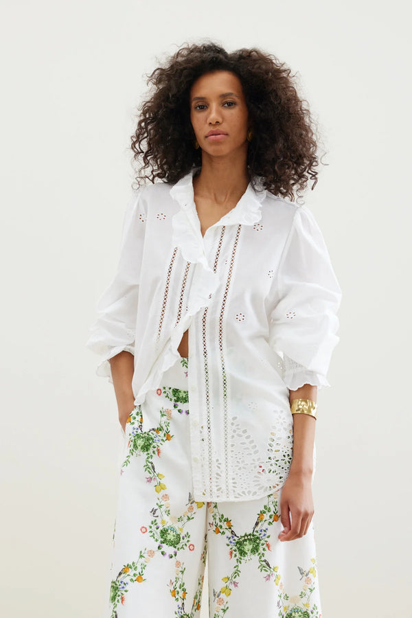 The Zicatela Shirt from Binny is a lightweight white cotton voile shirt with intricate hem embroidery, gently shirred sleeves and sweetly ruffled lapel. 