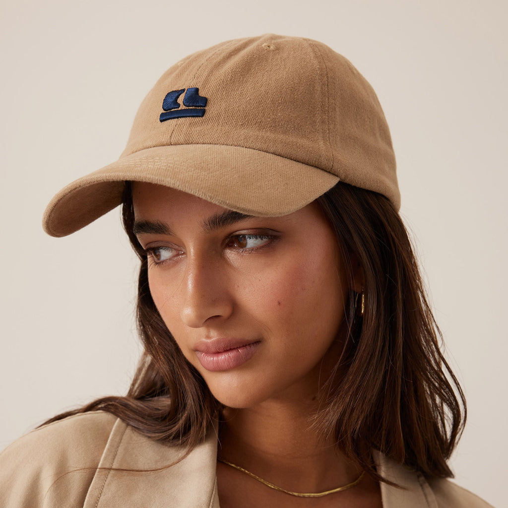 Woman wearing a beige cap and jacket with a neutral background