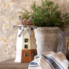 Decorative windmill and potted plant on a wooden surface with a stone wall background