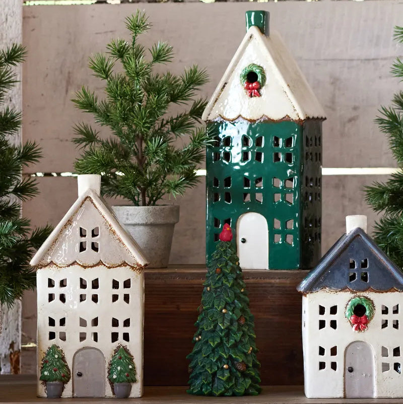 Decorative ceramic houses with Christmas trees and red holly berries on a wooden surface.