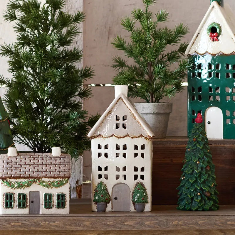 Decorative house-shaped lanterns and Christmas trees on a wooden surface.