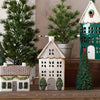 Decorative house-shaped lanterns and Christmas trees on a wooden surface.
