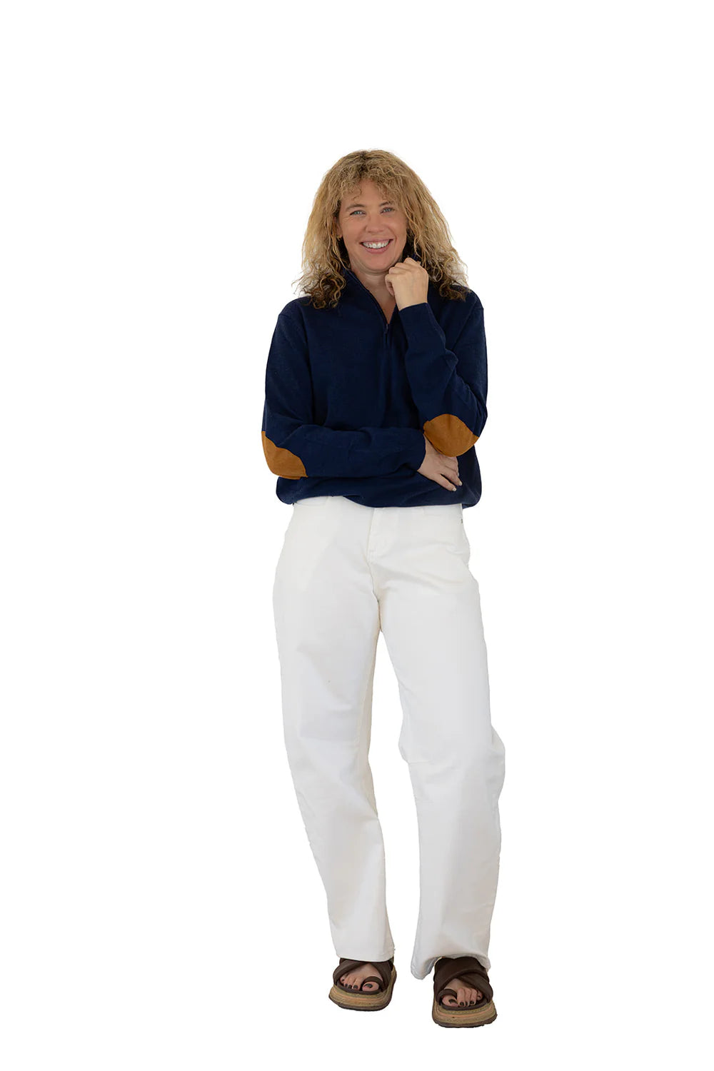 Woman wearing a navy sweater with brown accents and white pants on a white background