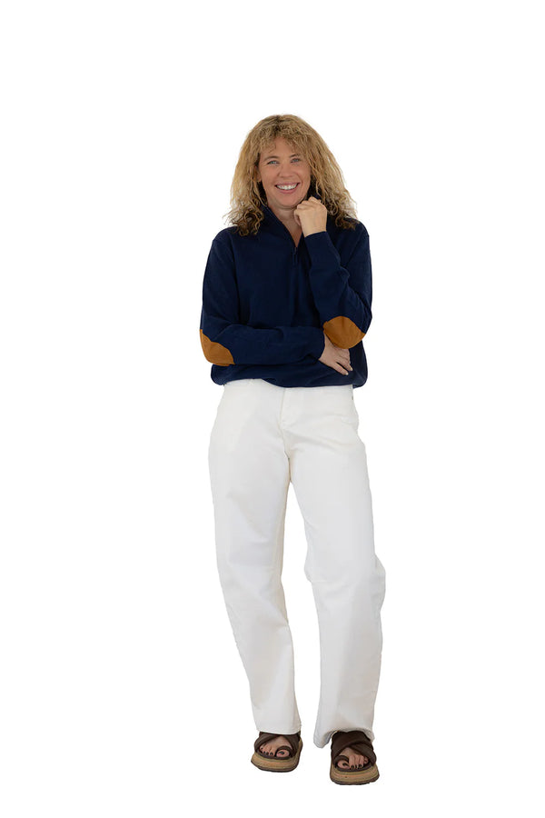 Woman wearing a navy sweater with brown accents and white pants on a white background