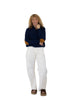 Woman wearing a navy sweater with brown accents and white pants on a white background
