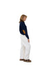 Woman wearing a navy sweater with a brown patch and white pants on a white background
