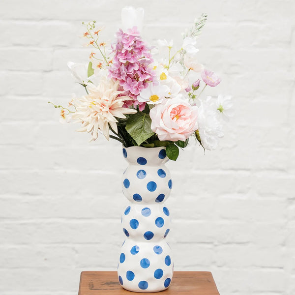 White vase with blue polka dots holding a bouquet of flowers on a wooden surface.