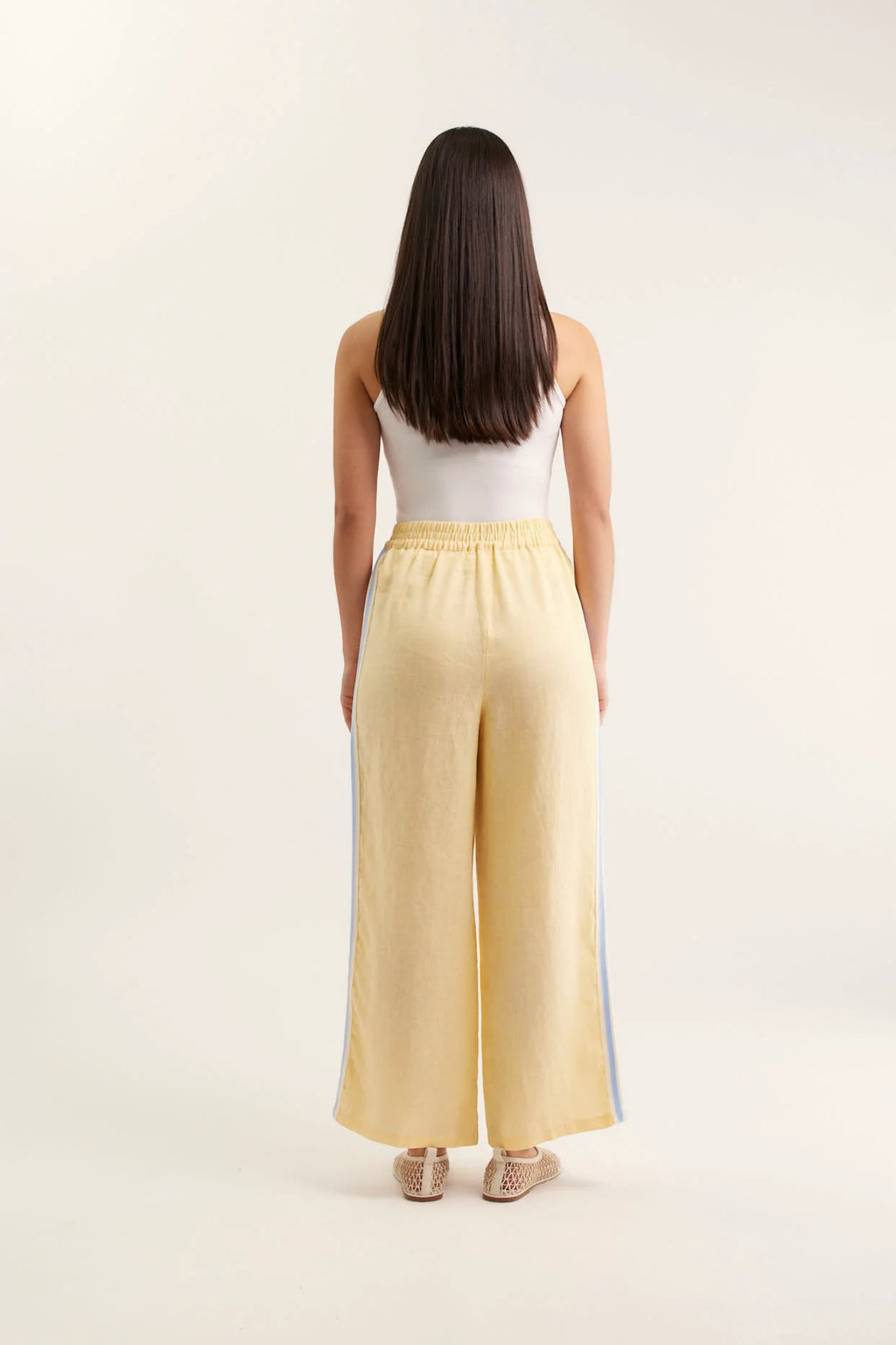 Woman wearing yellow wide-leg pants and a white top on a beige background