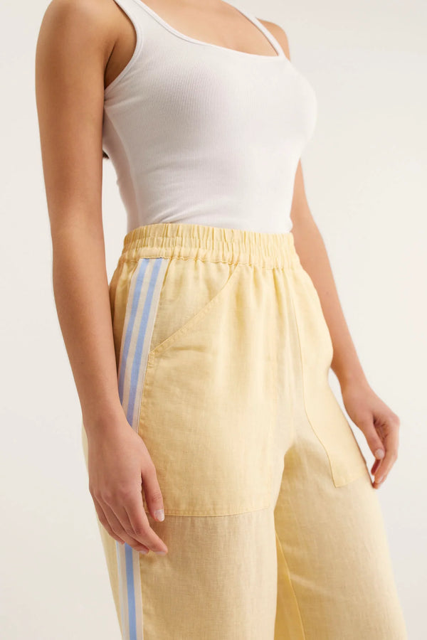 Person wearing a white tank top and yellow pants with blue stripes on a plain background